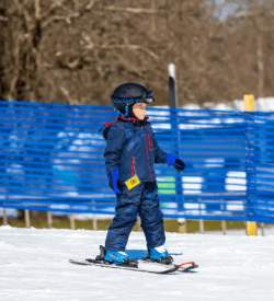 Small child in snow gear skiing down a hill at a ski resort