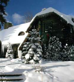 A front yard of a rustic mansion with everything covered in snow on a sunny day.