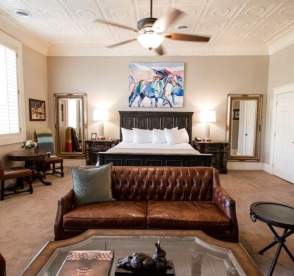 Modern hotel room with bed, couch, side tables, and beautiful artwork over the bed.