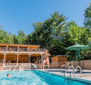 Huttopia Adirondacks swimming pool with person jumping into the water and hotel balcony in background