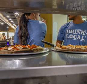 Pizza in a service window with staff in the background