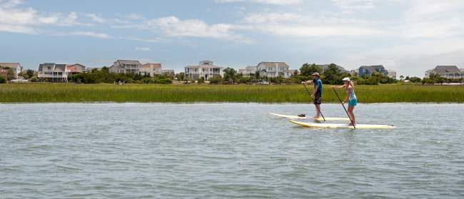 a couple paddleboarding in the marsh