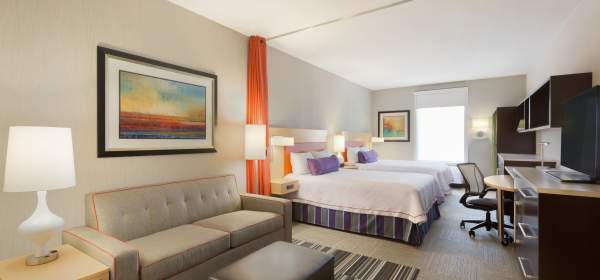 A hotel room with two queen beds, a couch, large work space, and TV is ready to welcome you in Fort Smith.