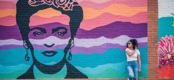 Woman leaning on the wall next to the Frida Kahlo mural in downtown Beaumont