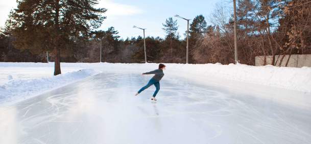Figure skater performing on an outdoor ice rink surrounded by a snowy outdoor scene.