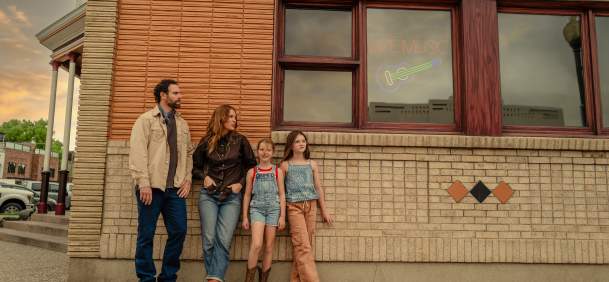 A family stands outside a downtown business in Cody, Wyoming, beneath a neon “Live Music” sign. Western-inspired clothing, cowboy boots and the historic streetscape reflect Cody’s family-friendly atmosphere, local culture and Western heritage.