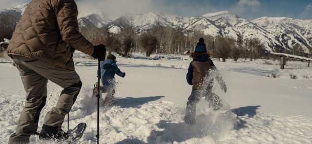 A group snowshoes through deep powder near Jackson, Wyoming, with snow-covered mountains rising across the horizon. The winter landscape and fresh snow highlight family-friendly snowshoeing and outdoor recreation in Teton County.