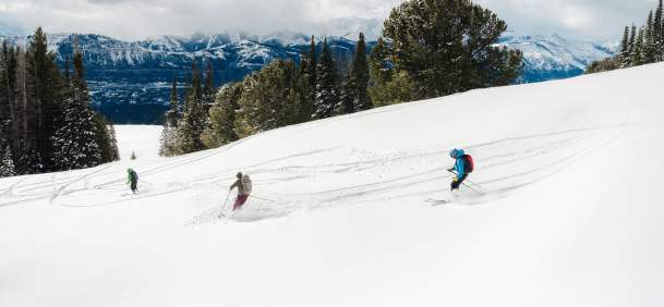 Three people backcountry skiing through snowy terrain in the Absaroka Mountains, Park County, Wyoming.