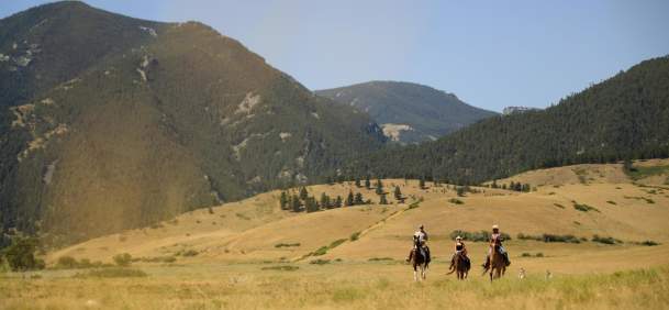 Horseback riders in grassy field with mountain ranges in the background.