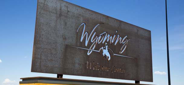 Bronze Wyoming welcome center sign set against clear blue sky.