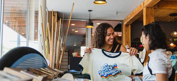 Shoppers holding up Wyoming shirt in store featuring clothing and outdoor-themed merchandise.