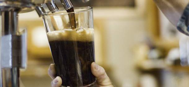 Hands pouring a dark craft beer from tap.