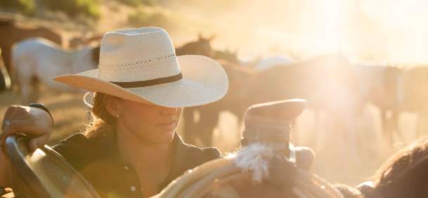 Cowgirl next to a horse and saddle at sunset.