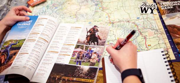 Travel Guide and map laid out on a table with person planning to write in book.