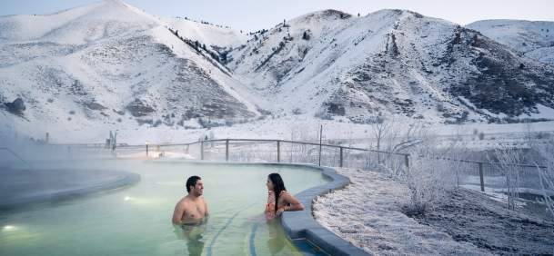 Steam rising from a natural hot spring with people soaking surrounded by snowy landscapes at Astoria Hot Springs Park in Wyoming.