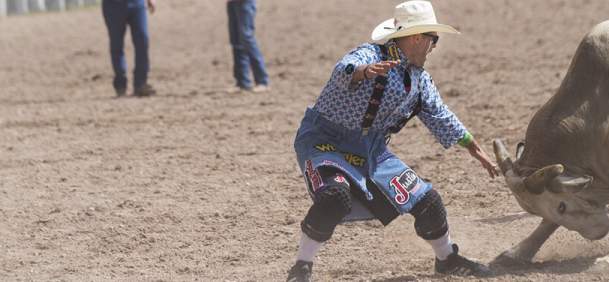 Rodeo clown facing off with a bull in a rodeo arena.
