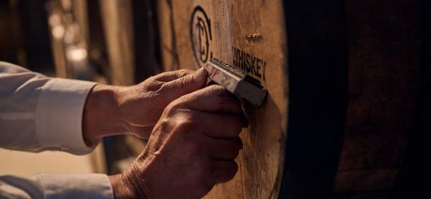 Wood barrel being stamped WHISKEY by pair of hands.