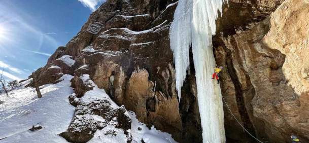 Ice climber scaling frozen waterfall against mountain.