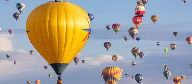 a ton of colorful hot air balloons float across a blue sky accented by white clouds