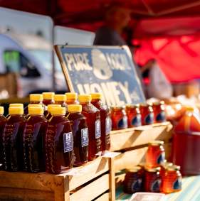 Bottles of honey are lined up on top of crates. There is a sign that has a bee hive in the middle and reads "Pure local honey."