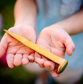 A golden spike from the Red River Railroad Museum Golden Spike Day Celebration held in a child's hands.