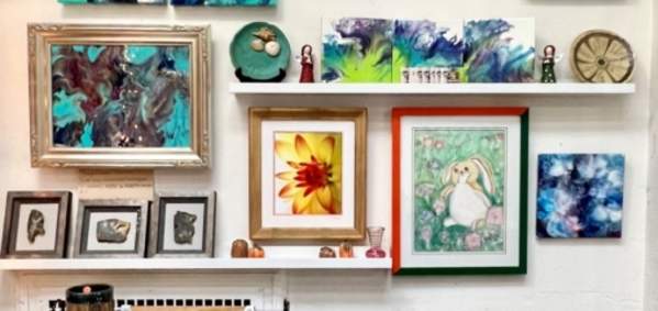 a variety of colorful artwork is displayed on a wall with ceramics on a rack below