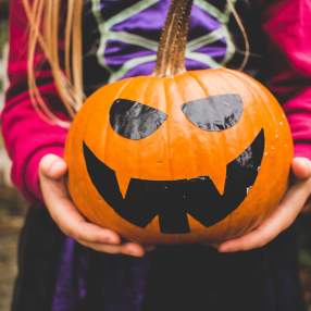 Hands of a girl holding a pumpkin with a painted face