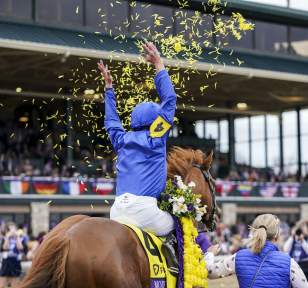 A jockey in blue and yellow silks celebrating a win atop a thoroughbred horse amidst yellow confetti at Keeneland.