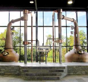 Two very large copper stills sit in front of a wall of windows at the Lexington Brewing and Distilling Co.