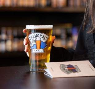 A Brewgrass Trail pint glass and guidebook sit on a table with a patron.