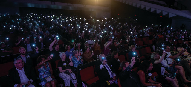 a large crowd using their cell phone flashlights in a dark auditorium