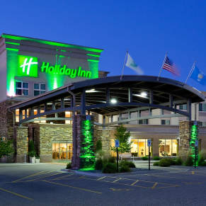 Square image of Holiday Inn from the outside at dusk with green light up sign brightening the image