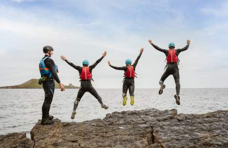 Group of people coasteering and jumping into water while instructor watches on