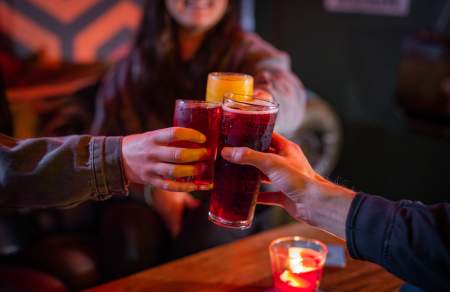 Three people clinking glasses in a dimly lit bar.