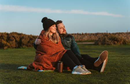 Young couple under a blanket with a coffee watching a sunset at rhossili bay in the winter