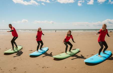 A family of four standing on surf boards on the sand practicing moves.