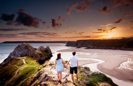 couple holding hands looking out over three cliffs bay with the sun setting