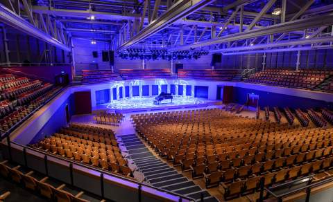 A large event venue with modern wooden effect seating and large lit stage with piano