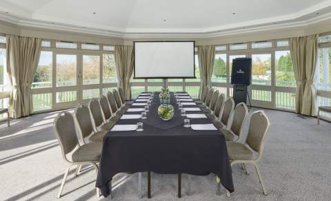 A long boardroom table in a premium room, surrounded on three sides by large windows.