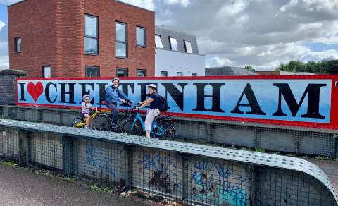 A family cycling past a Cheltenham sign.