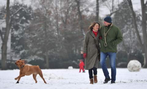 Visitors walking their dog through a snow filled park in Cheltenham