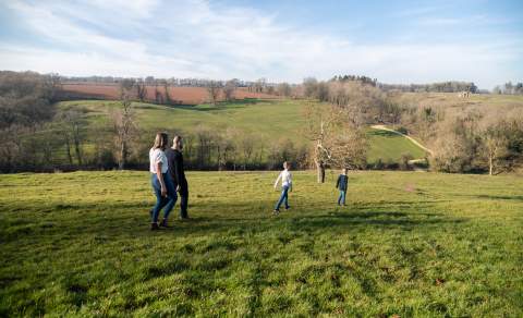 Two boys walk ahead of their parents across a field near Blockley, with trees and hills in the distance.
