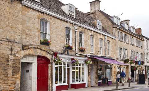 A couple walking past shops with pretty frontages and hanging baskets in Chipping Norton town centre