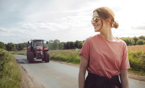 Woman in sunglasses with a tractor in view behind her