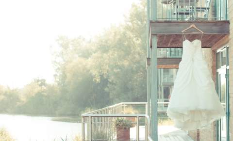 A wedding dress hangs from a balcony overlooking a lake at De Vere Cotswold Water Park