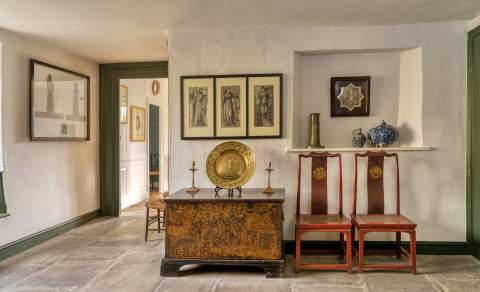 The Garden Room at Kelmscott Manor with William Morris artefacts in view: two Arts & Crafts chairs beside a chest and drawings on the wall