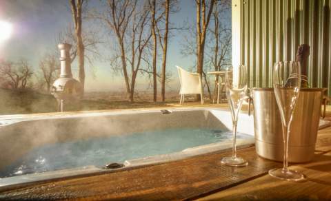 Hot tub bath at the Hilly Huts on FArncombe Estate. Steam rising from tub with bottle of sparkling wine, glasses and chimnea in background
