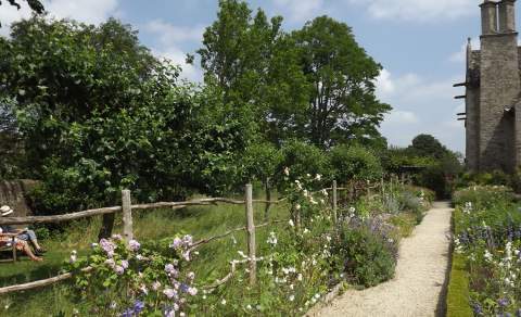 Two people sitting on a bench in the garden at Kelmscott Manor. A fence made of fallen wood from trees on the estate lines the gravel pathway.