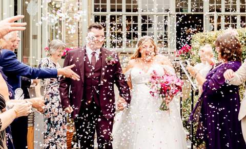 Friends and family throw confetti over a smiling bride and groom