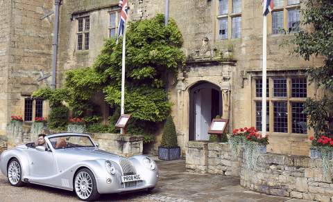 A vintage car parked in front of the Cotswold stone entrance to The Lygon Arms Hotel in the Cotswolds